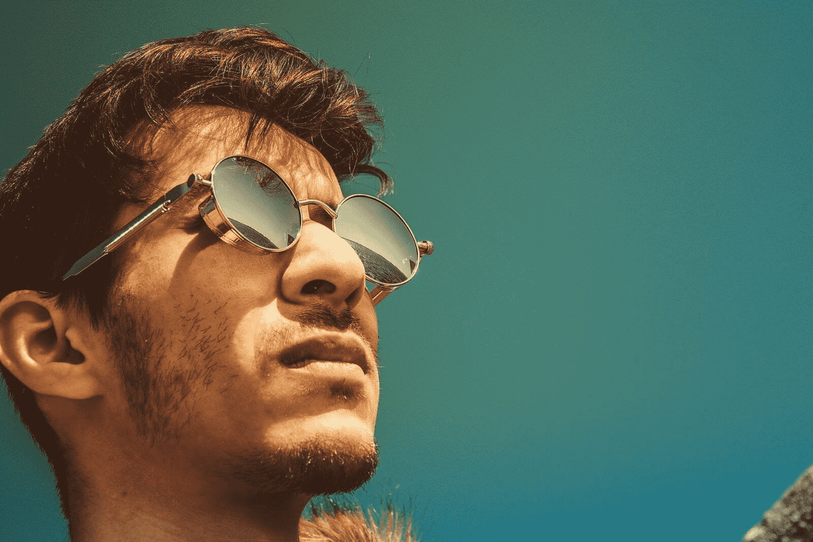 Man with teal background and dark sunglasses, looking off into the distance with hope and determination.