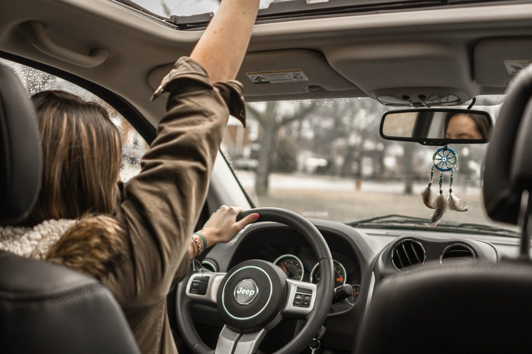 Picture of a woman raising her arm in celebration as she drives her car.